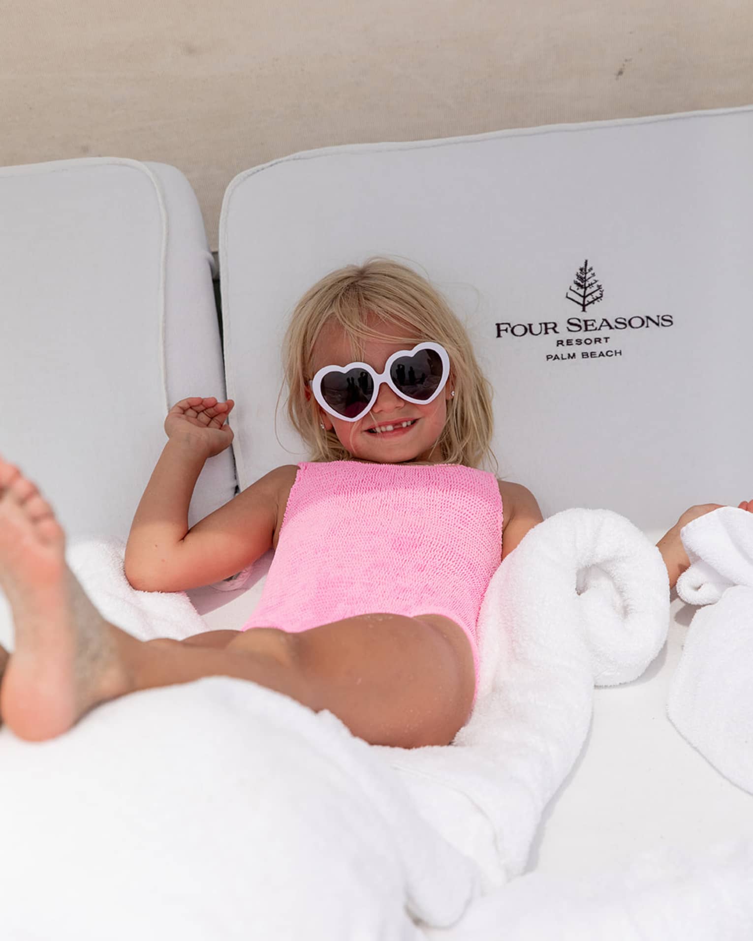 Young guest wearing heart-shaped sunglasses laying on a lounge chair.