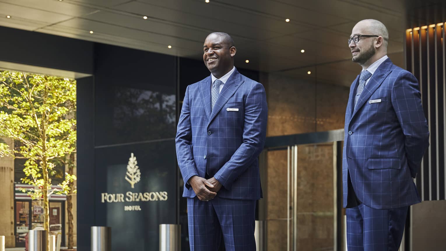 Two men in suits waiting outside of a Four Seasons Hotel entrance.
