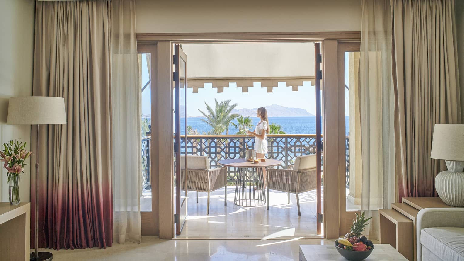Woman stands on sea-view balcony connected to a hotel suite