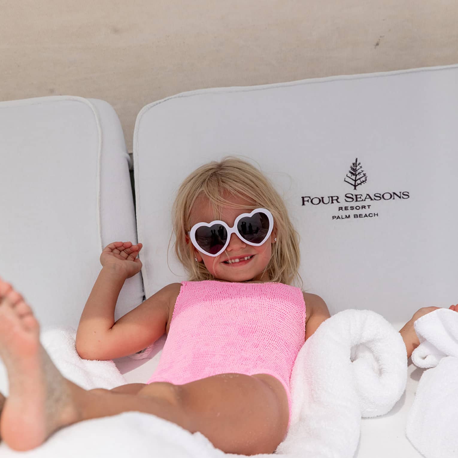 Young guest wearing heart-shaped sunglasses laying on a lounge chair.