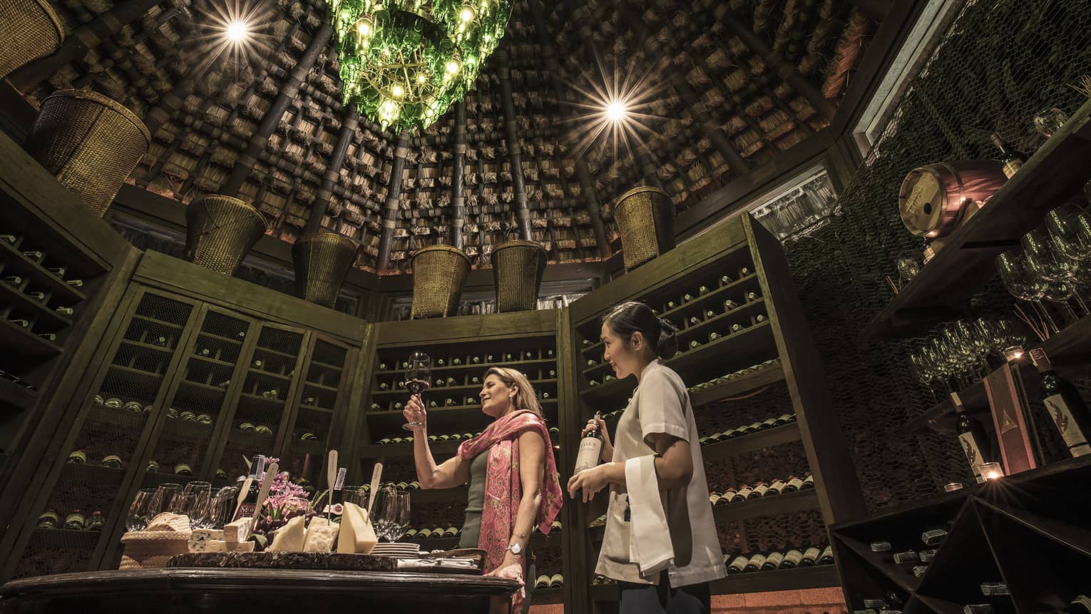 Two people in rustic wine cellar with a green bottle chandelier