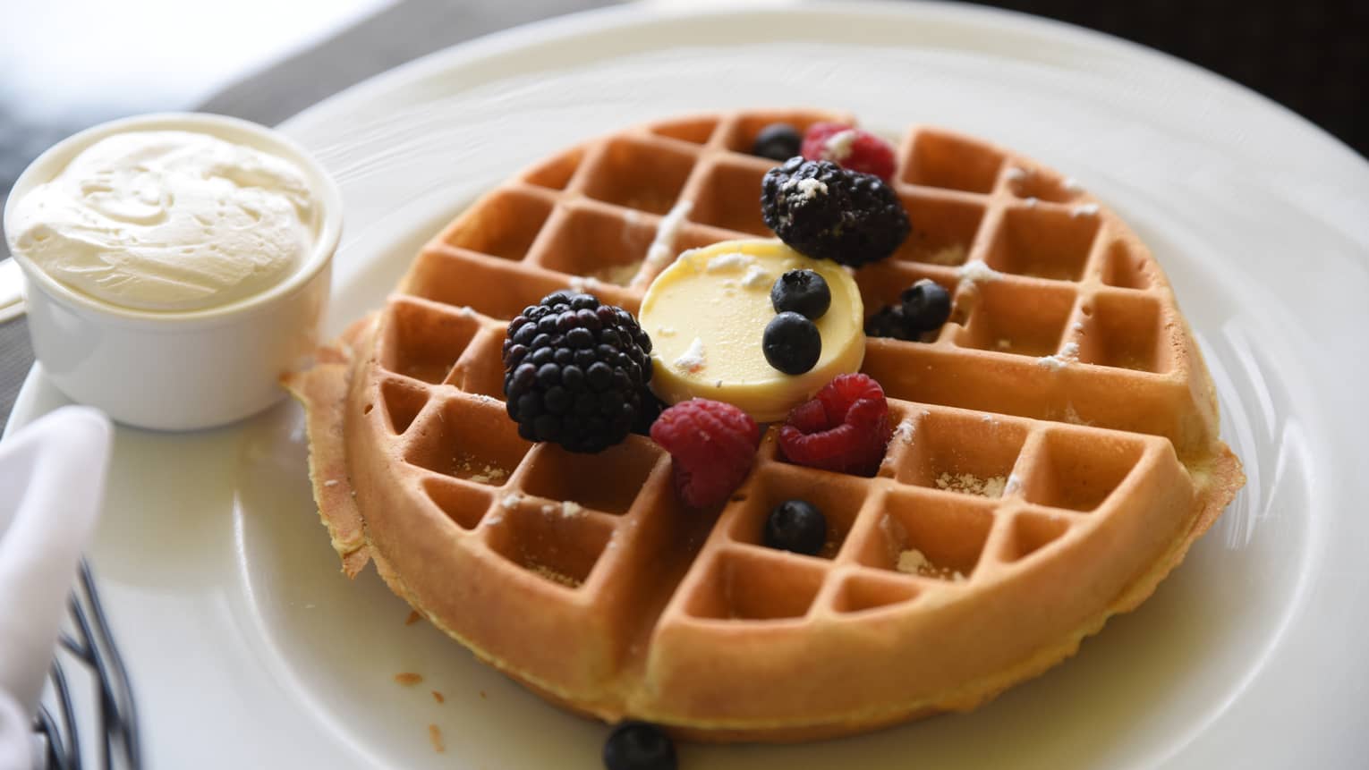 Waffle with butter and sprinkle of fresh berries, cup of whipped cream on plate