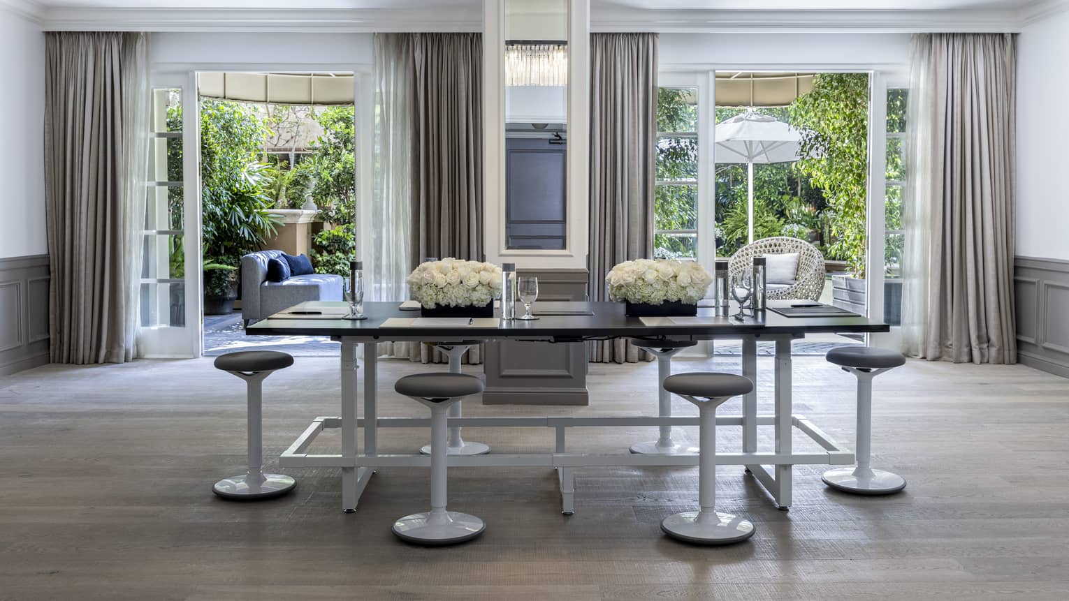 A meetings room with a large table surrounded by stools and large open windows in the background.