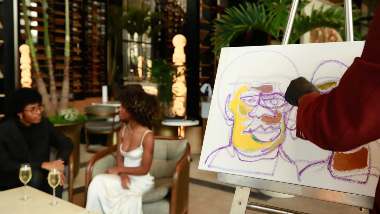 Two people enjoying wine while having a colourful portrait drawn of them.