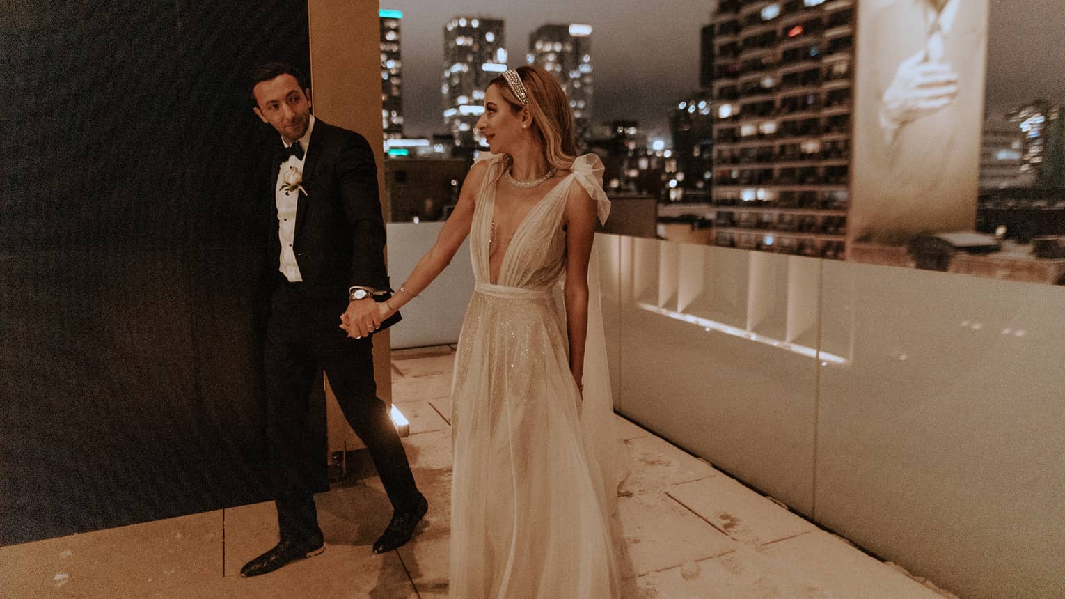 Bride and groom walk hand in hand on a rooftop terrace in Montreal, with the city skyline in the background