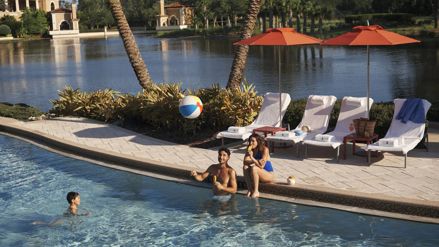 Two adults play with kid and a beach bar in the family pool at luxury resort