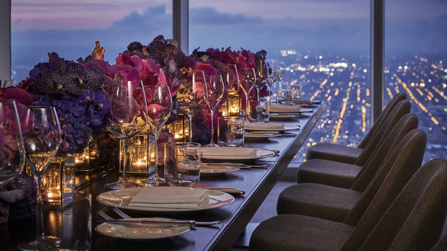 A banquet style table is decorated with tea candles, white plates, pink flowers and overlooks downtown Philadelphia 