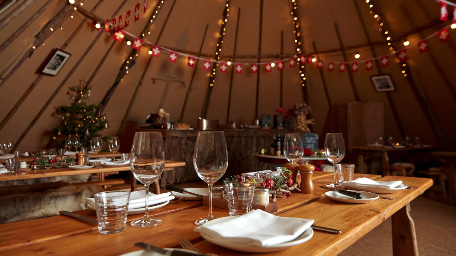 Holiday-decorated yurt with set wooden tables and string lights