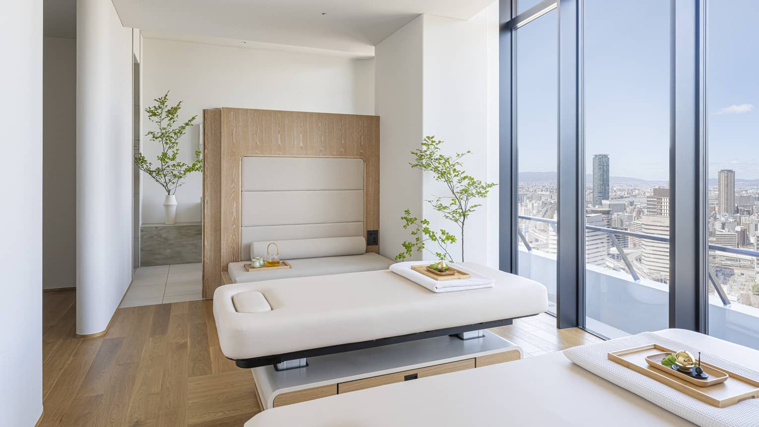 Spa treatment room with two treatment tables and wall of windows overlooking city at The Spa at Four Seasons Hotel Osaka