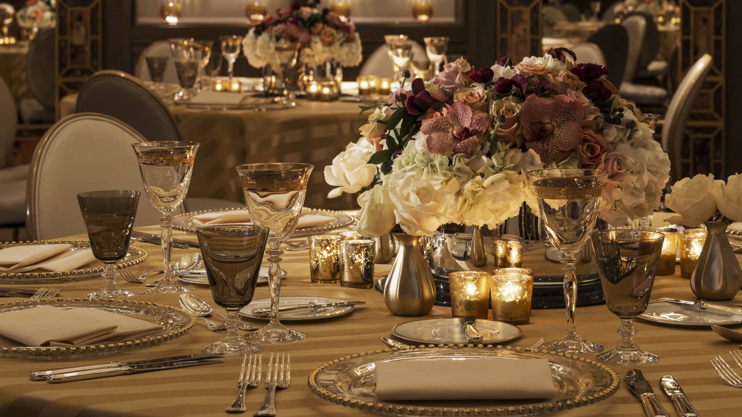 Gold candles and glassware, white and pink floral arrangement on wedding banquet table