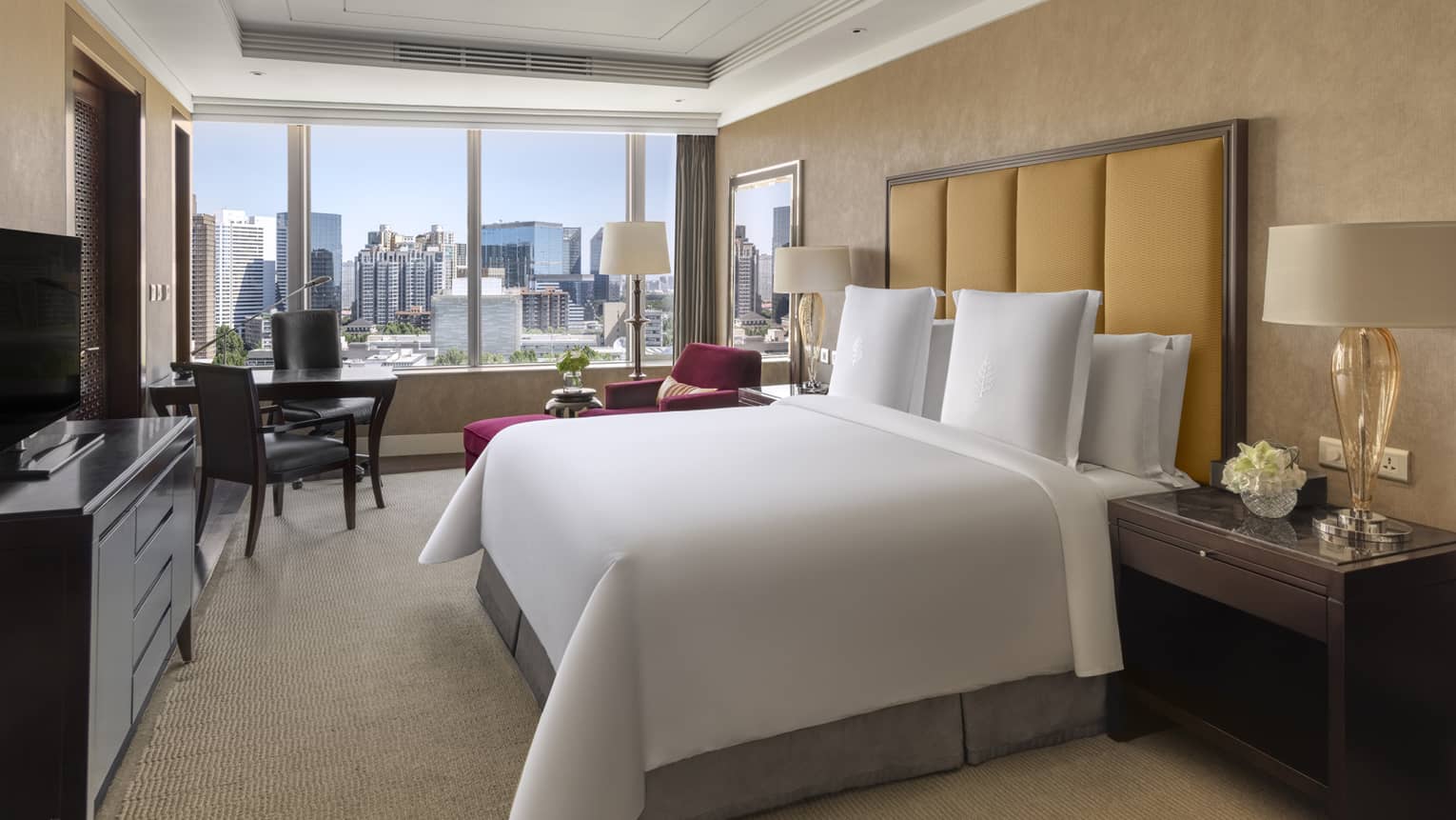 Hotel room with king bed, tan headboard, desk with two chairs, dresser and window-side chaise