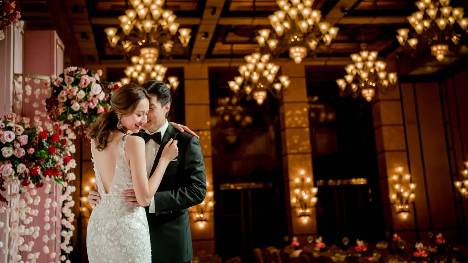 Bride and groom embrace at wedding ceremony in banquet room with lights