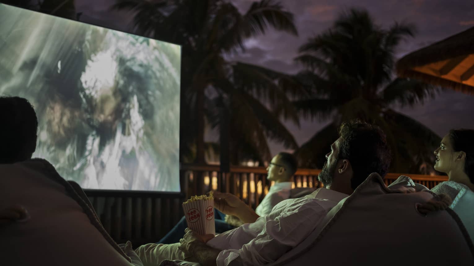 Group of people sit on bean bags with popcorn watching movie under the stars 