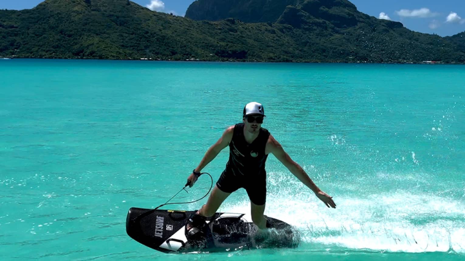 Person on JETSURF board rides on turquoise water, mountain visible in background