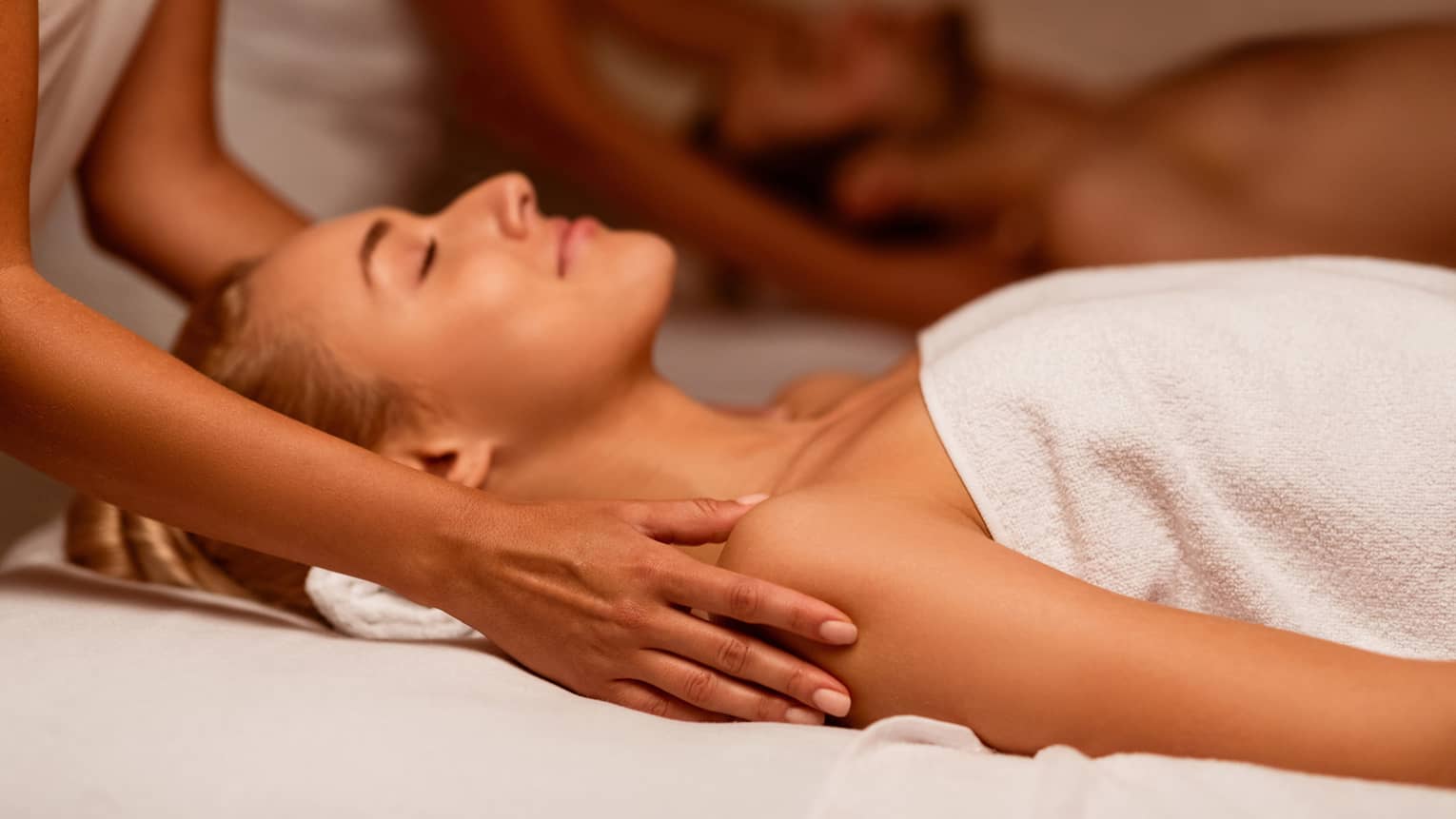 Two spa therapists perform a couples' massage