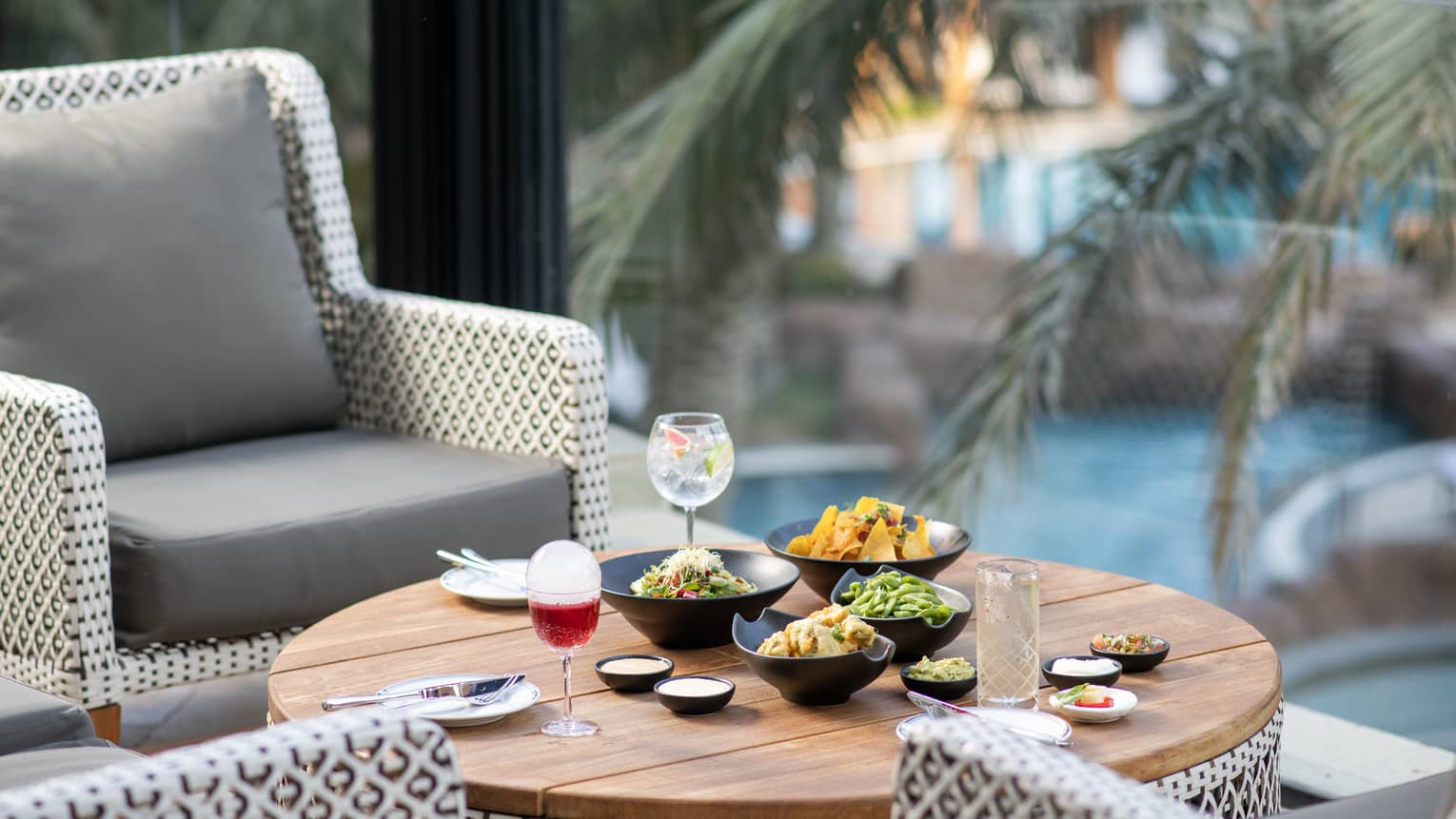 An assortment of food in black bowls and cocktails near a pool.