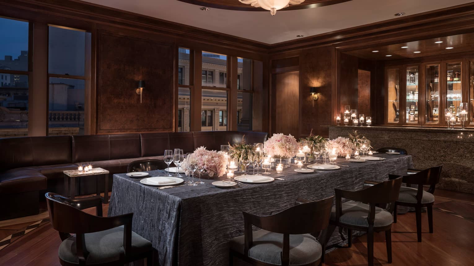 Elegant, candle-lit dining table in private den with grey tablecloth, pink flower arrangements, wine glasses
