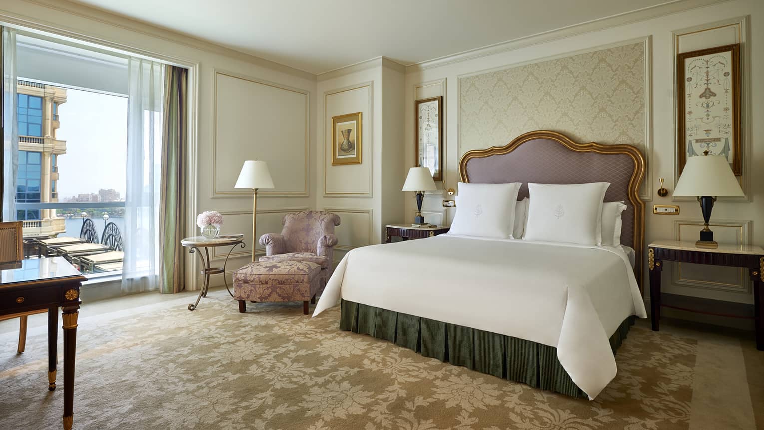 Superior Room bed with padded headboard with gold trim, pink satin armchair by patio door