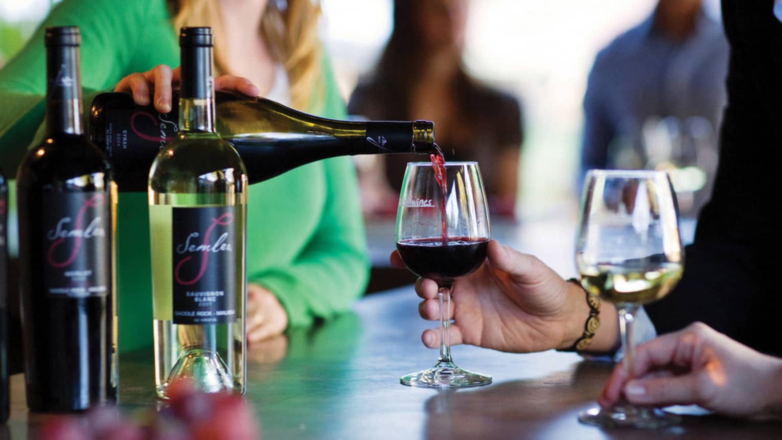 Woman pours red wine from bottle into glass at Malibu Coast tasting bar