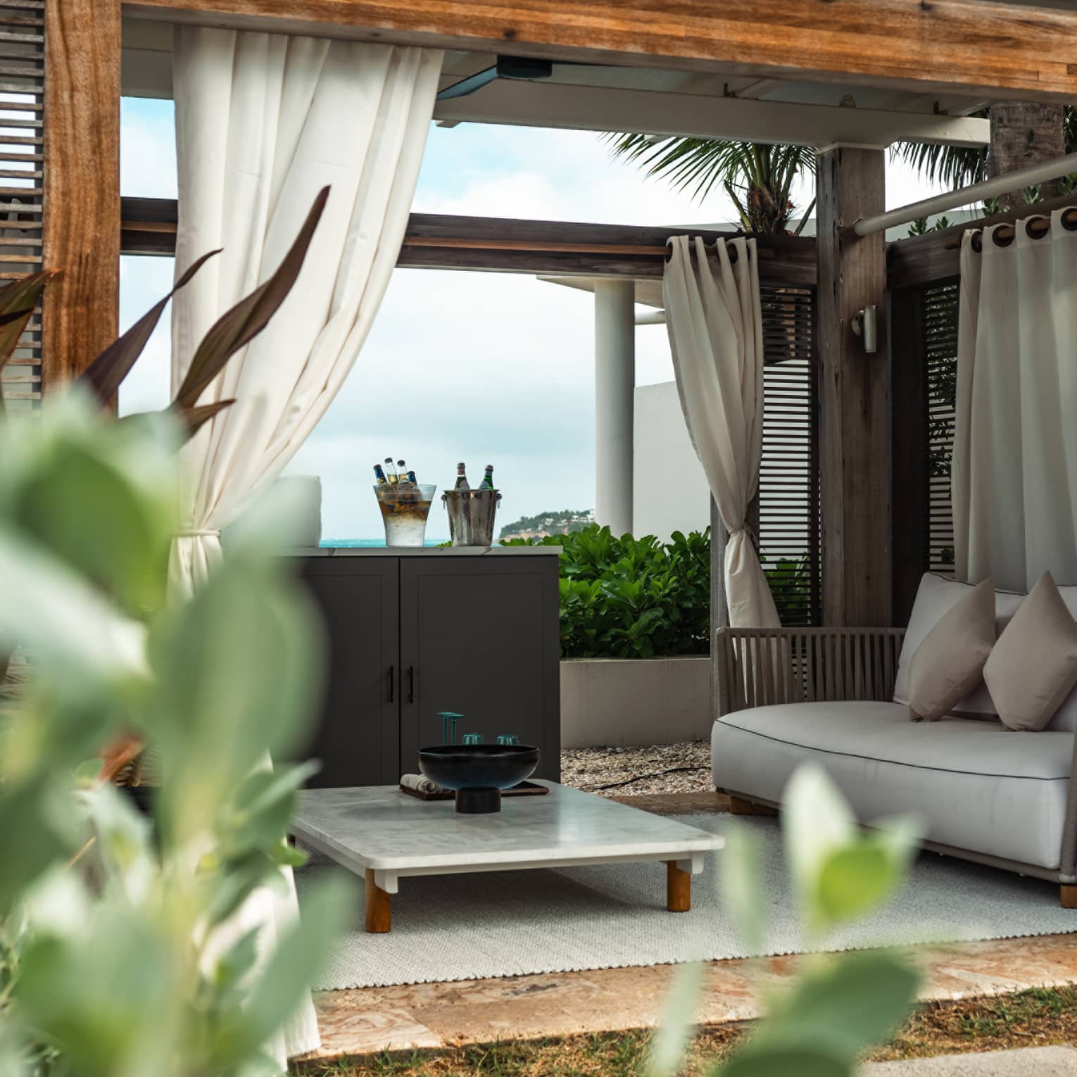 A cabana with a marble table and couch surrounded by palm trees