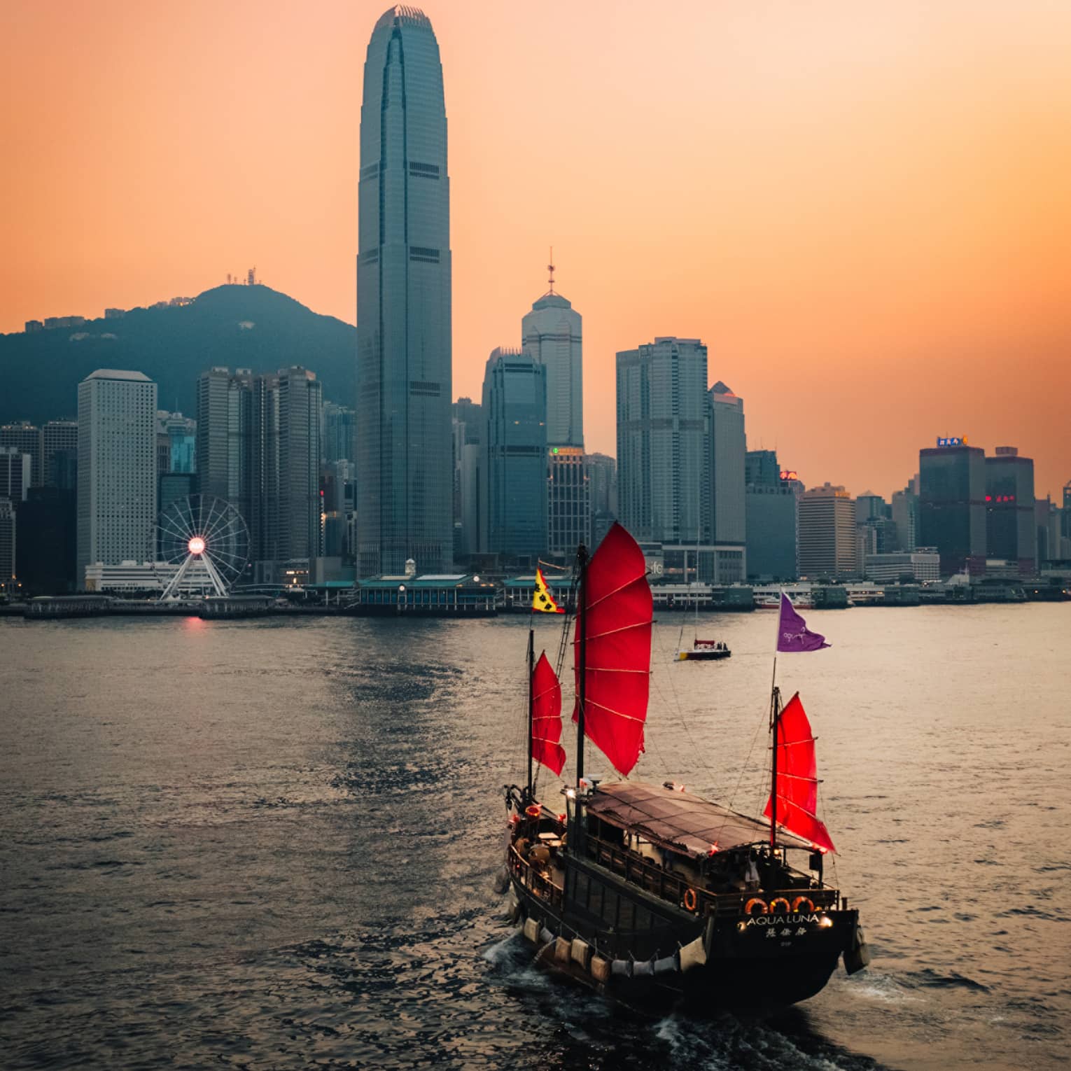 Boat with red sails on harbour in Hong Kong at sunset with city buildings at the shore