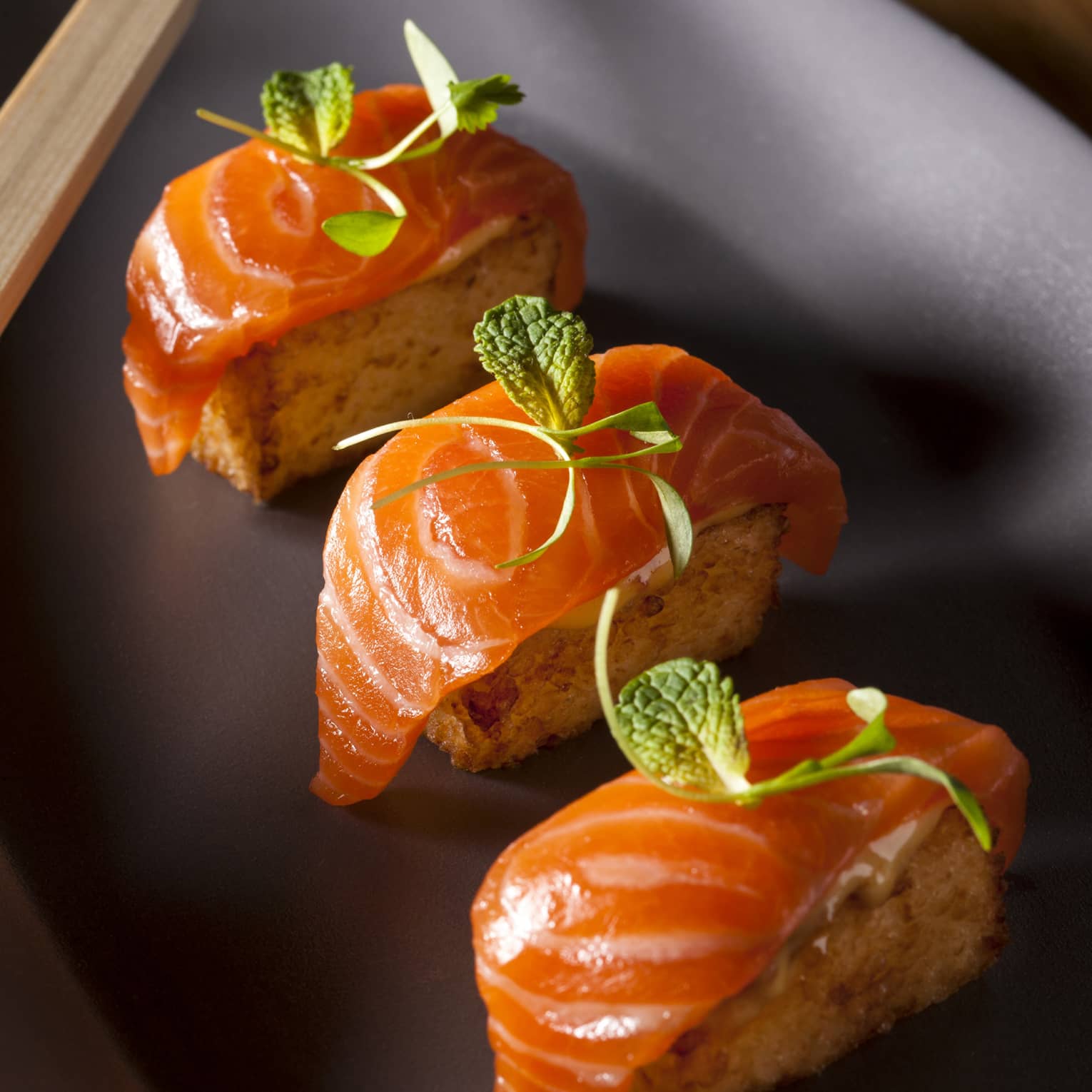 Three pieces of crispy salmon sushi on black platter