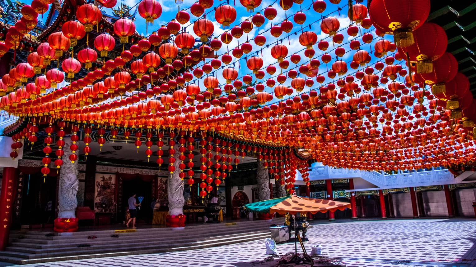A temple’s entrance features pillars embellished by intricate carvings. Hundreds of crimson red lanterns are strung overhead.