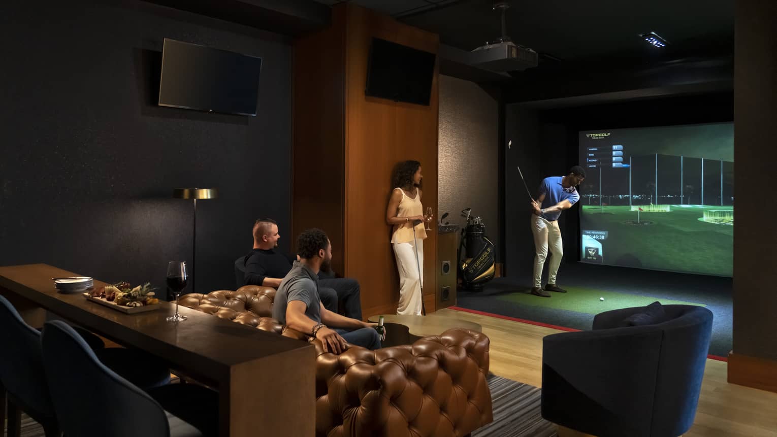 A group of people enjoying an indoor golf simulator experience at the luxury hotel Topgolf Swing Suite, with plush seating and a relaxed atmosphere