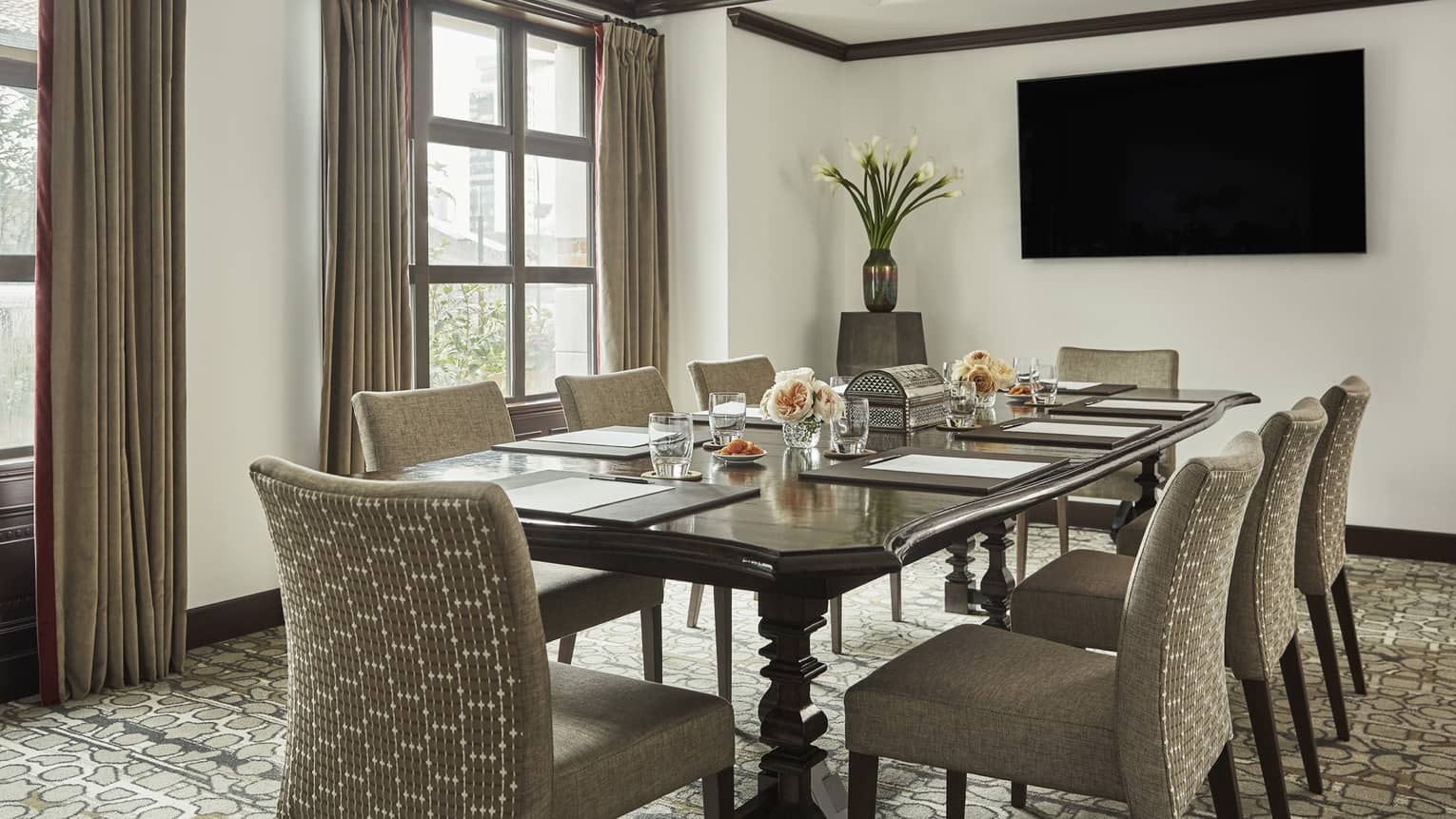 La Merced meeting room with small boardroom table, plush chairs by TV screen and sunny windows 