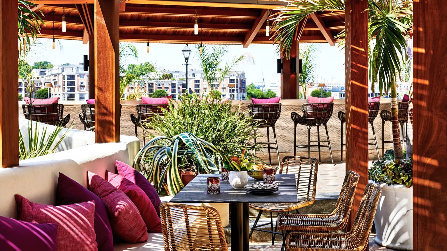 An outdoor eating venue with red cushions on benches and stools surrounded by red pillars and trees.