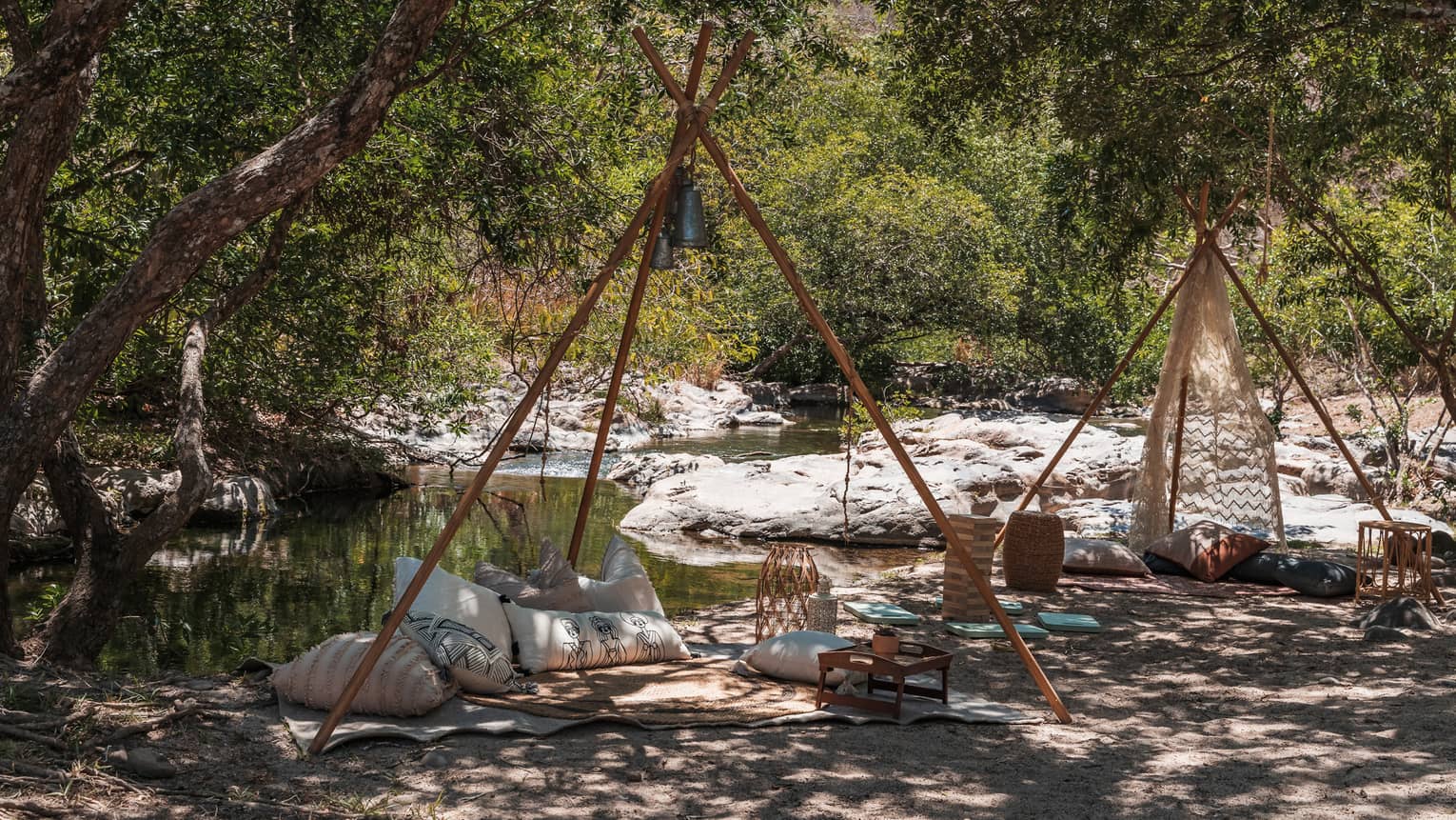 Two blankets with pillows and games set up by a creek