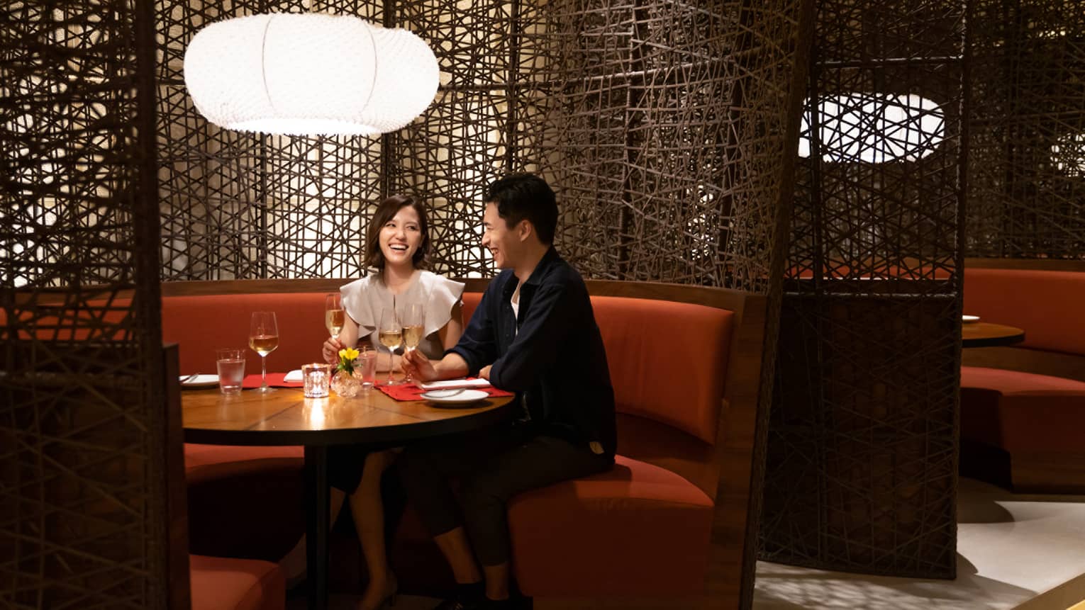 Woman and man smile at each other at rounded booth table in restaurant at Four Seasons Hotel Kyoto