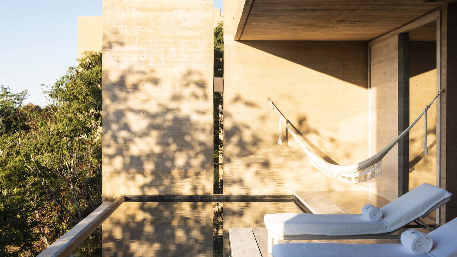 Private resort suite terrace with infinity pool, two lounge chairs and hammock