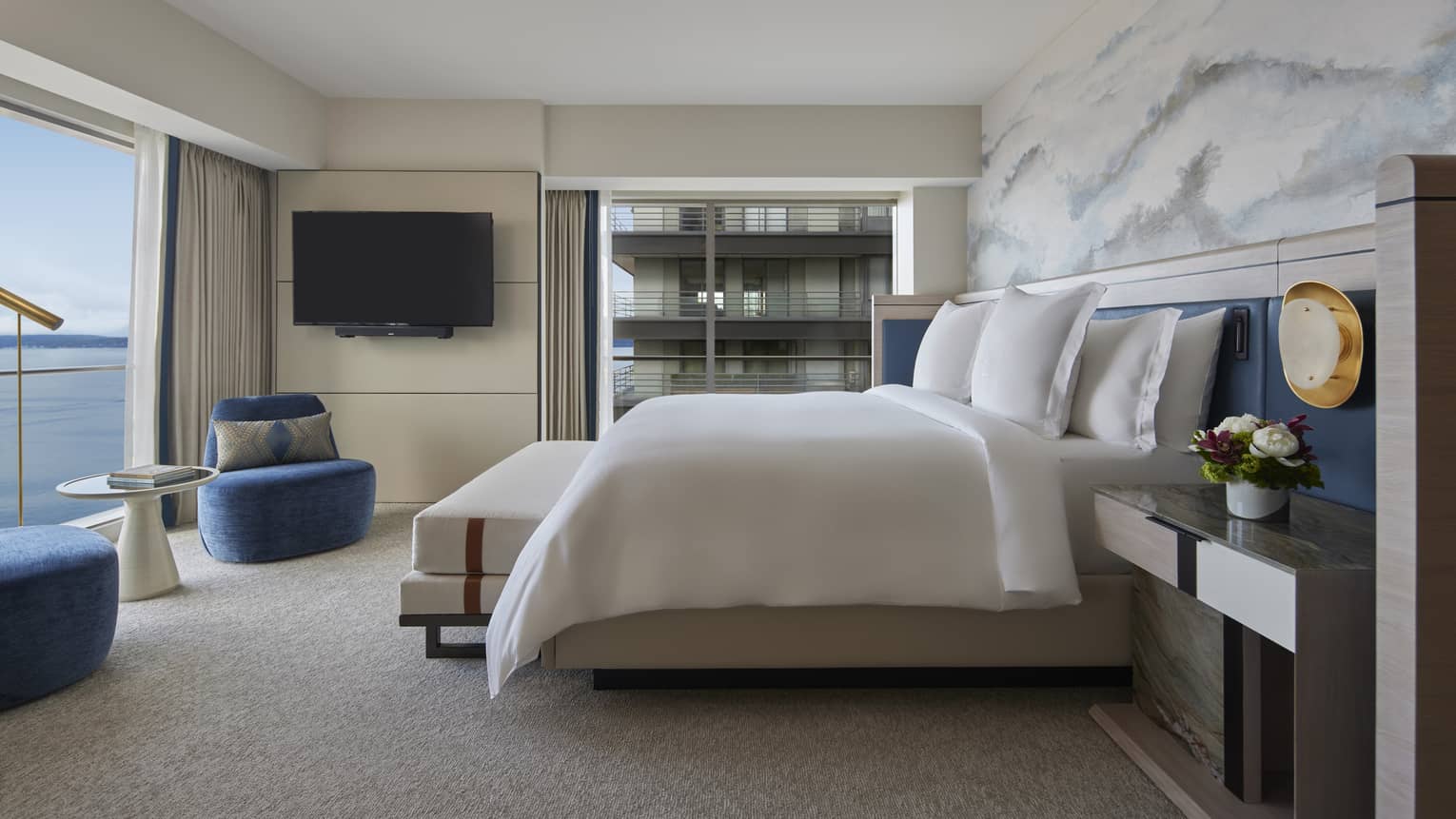 Bedroom with king bed, cloud-like accent wall, two royal blue chairs and wall of windows