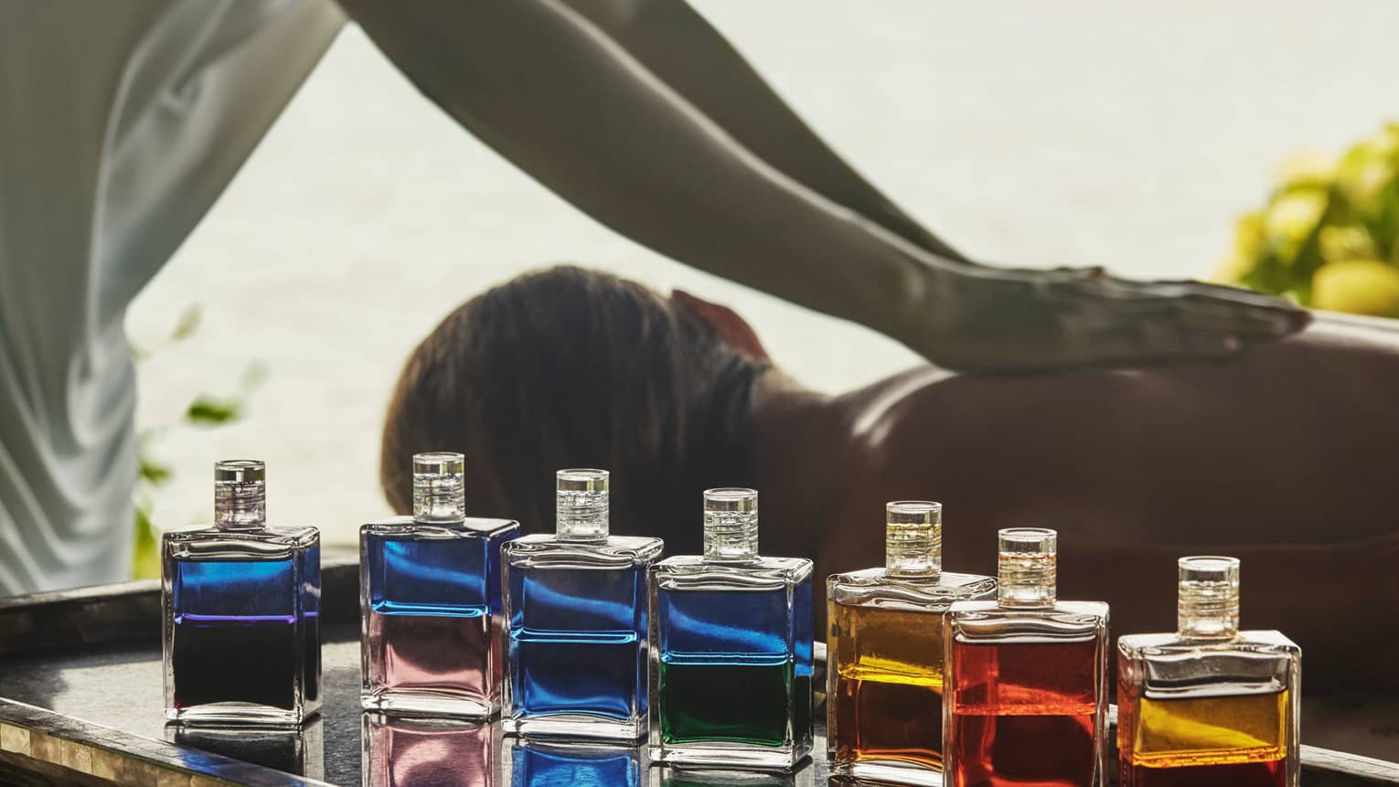 Spa staff massages woman's back behind row of colourful glass bottles with oils