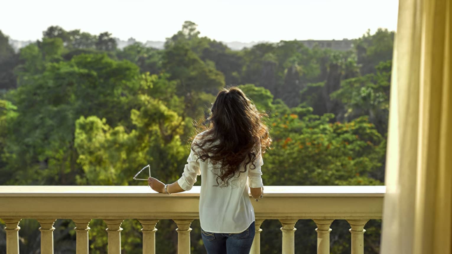 A woman standing on a large balcony looking out at a forest.