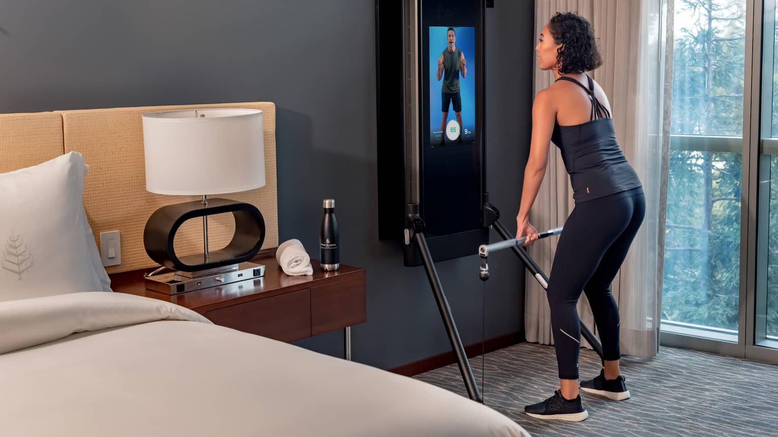 Woman exercises in front of an instructor on a screen in a Tonal technology-equipped guest room