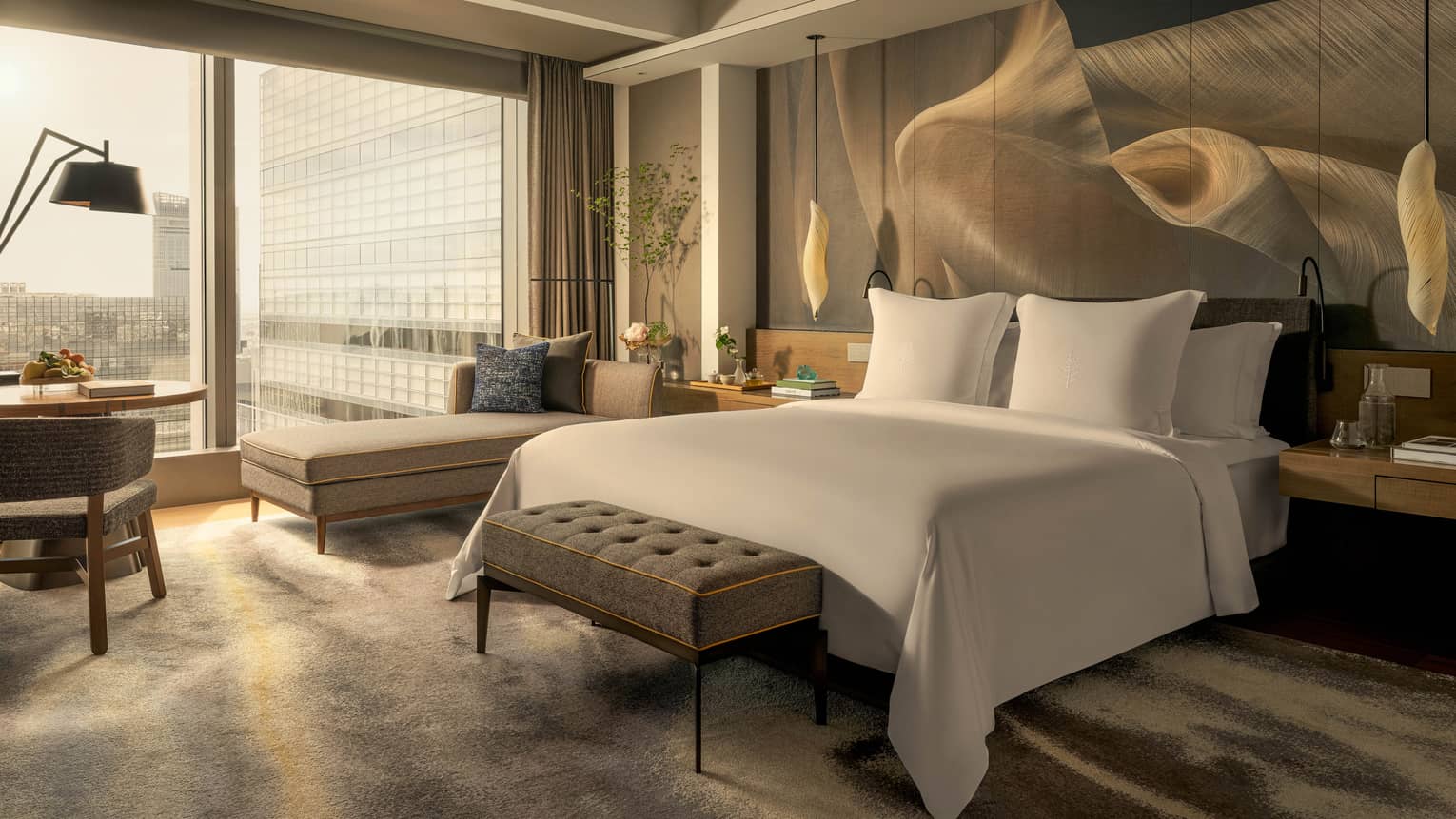 Luxury hotel room with king bed, chaise, hanging lights over bedside tables, and wall of windows