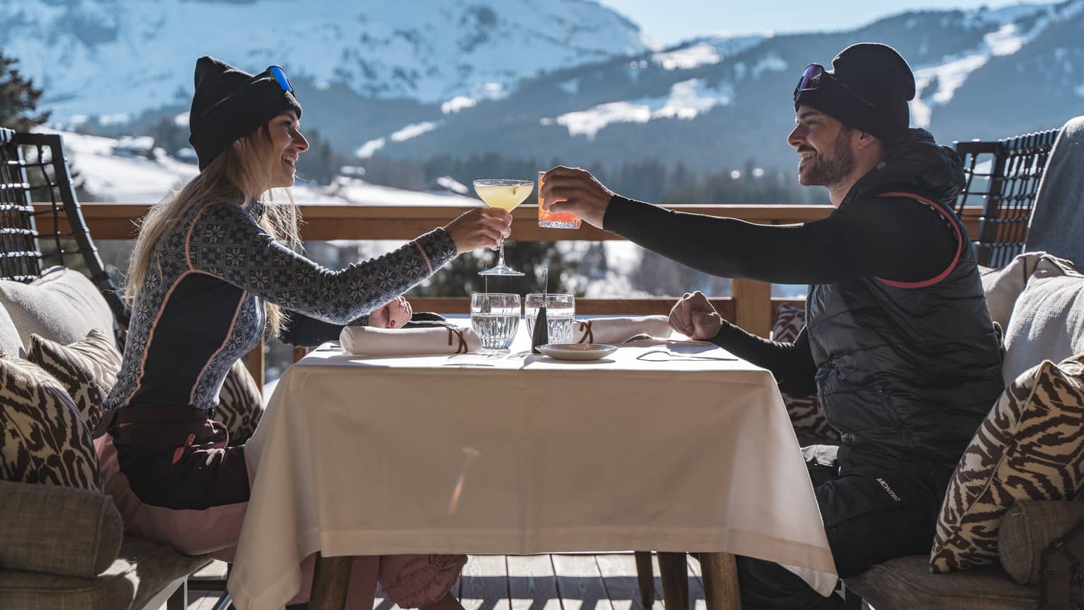 Two people drinking on a patio outside with snowy mountains in the distance