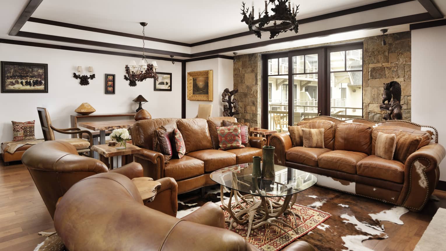 Mountain-chic living room with two brown leather sofas, two matching arm chairs, antler chandelier
