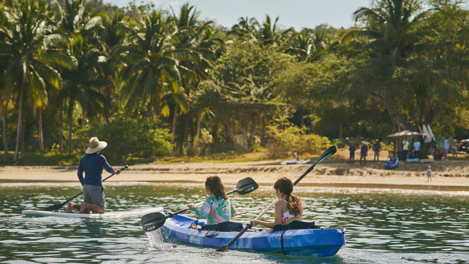 A group kayaking while a group watches from a beach.