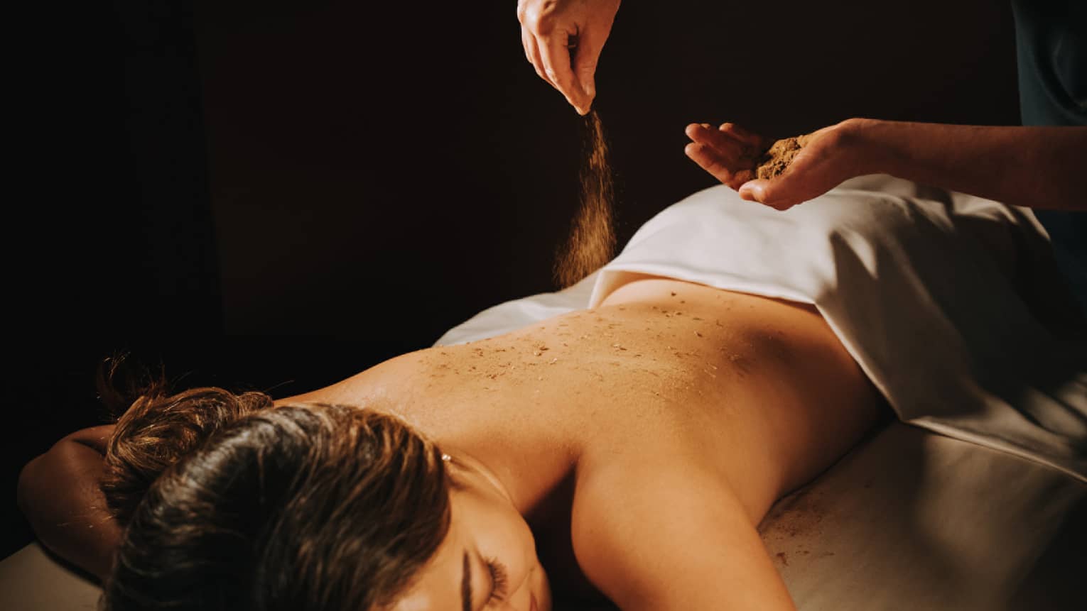 Spa staff sprinkled coffee powder over woman's bare back as she lays on massage table