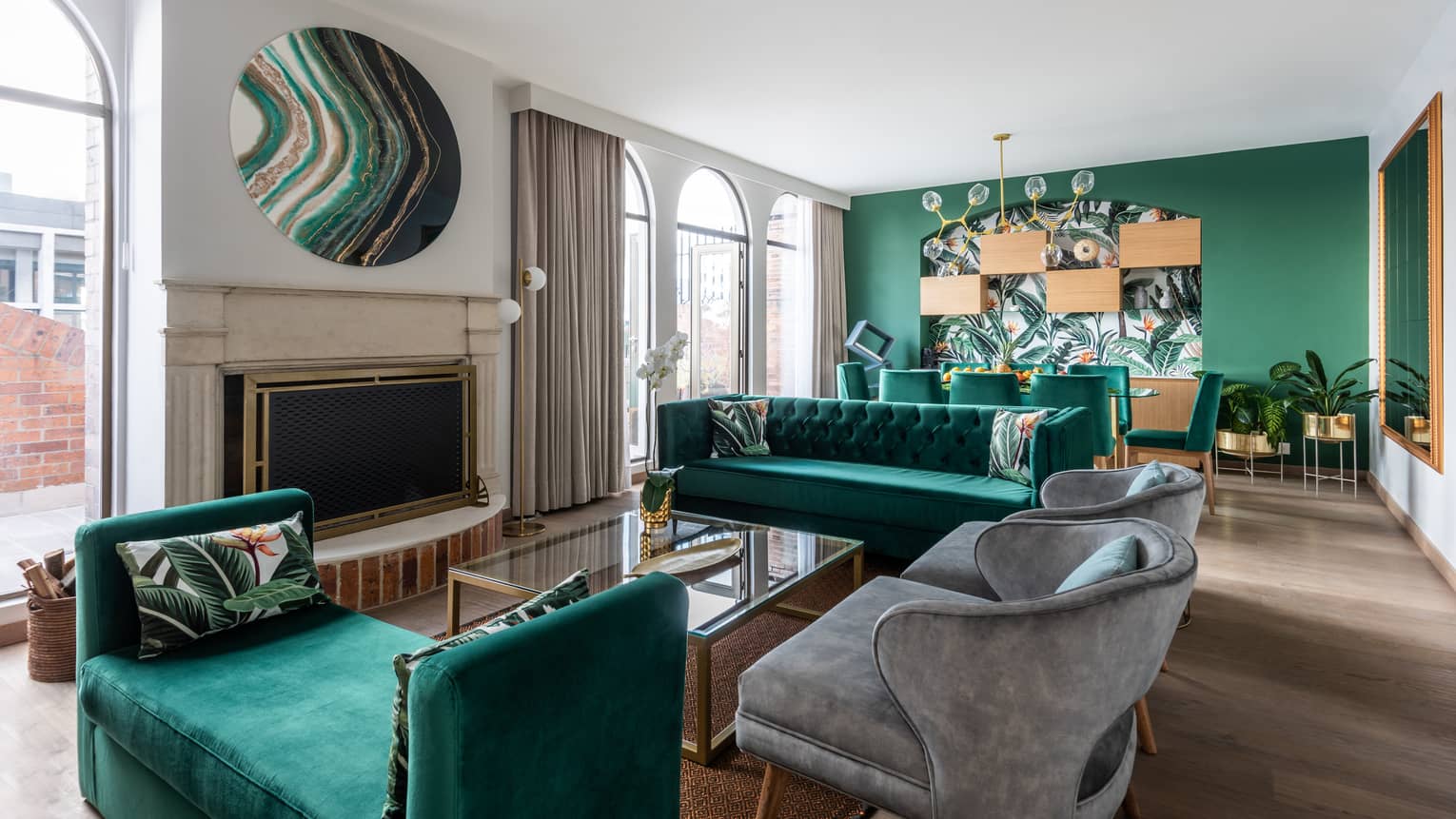 A sitting area with several emerald green couches, small grey chairs and plants.