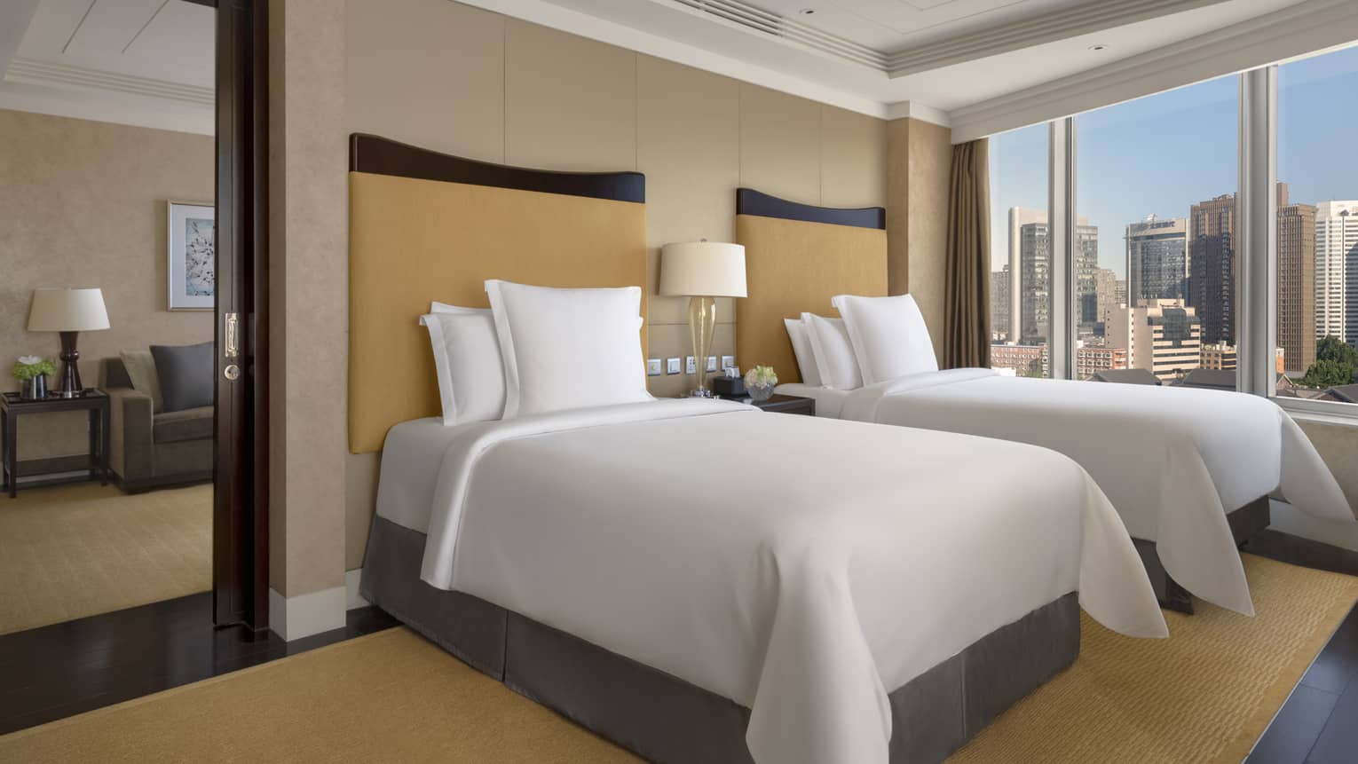 Hotel suite bedroom with two single beds, tan headboards and rug, wall of windows