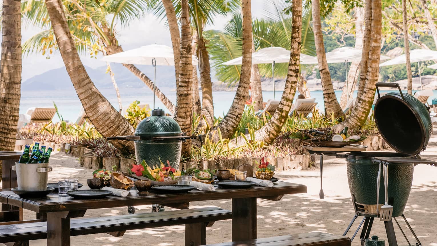 BBQ and grill equipment outside near a table and palm trees.