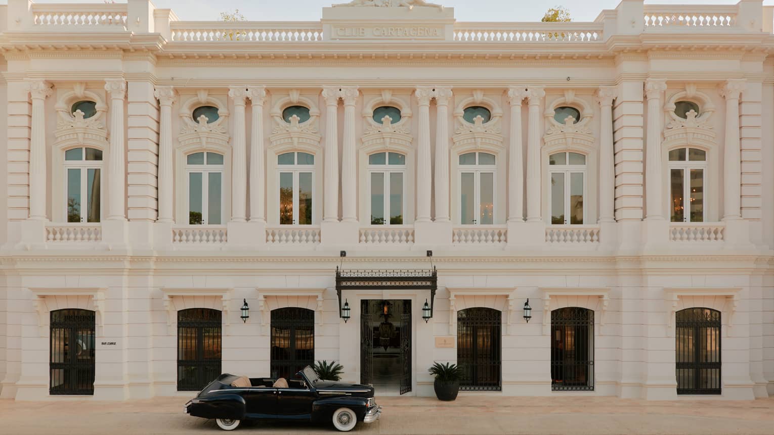 Exterior of a white stone Colonial-style hotel building with a vintage car out front