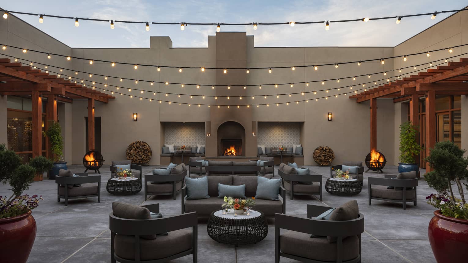 A courtyard area outside with many seats and small tables with fair lights hanging under an open sky.