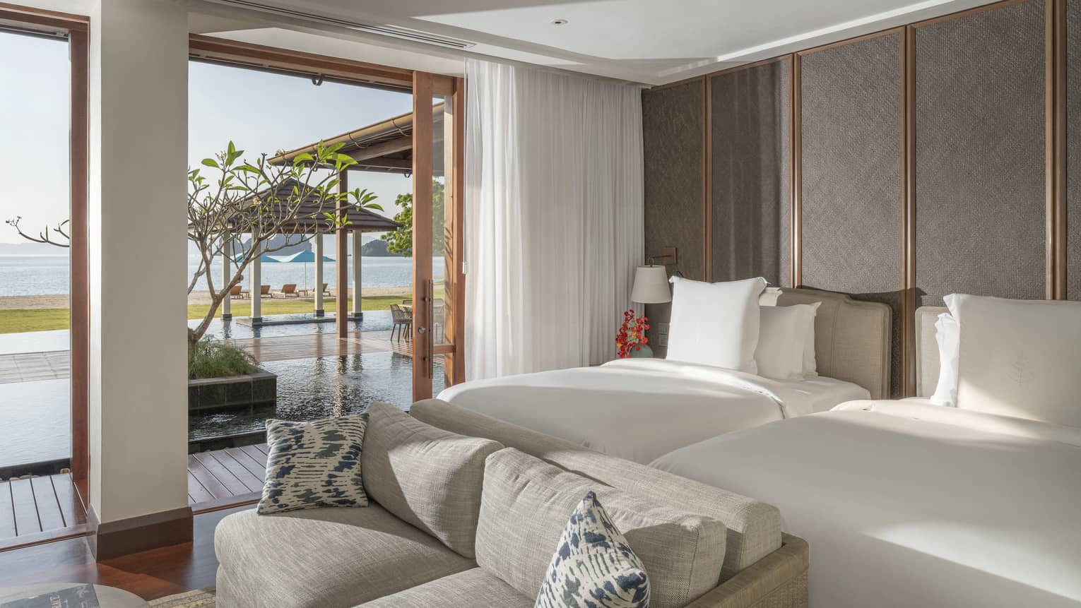 Bedroom with two beds, sofa and walk-out terrace to the pool and beach view