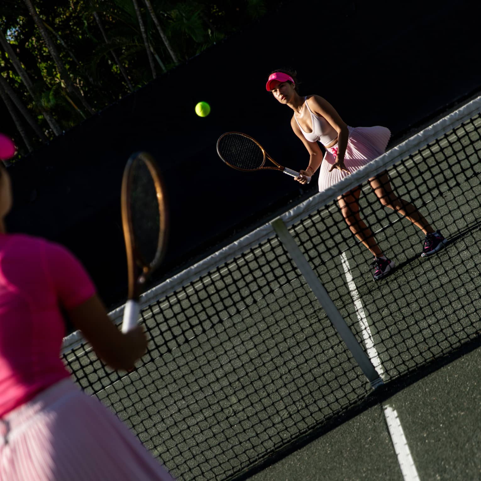 Two tennis players both wearing pink volley a ball over the net