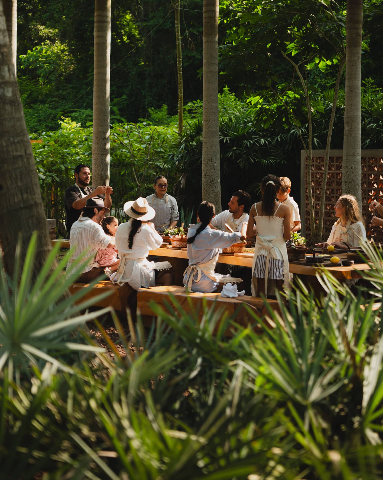 People seated around a long outdoor dining table set among palm trees